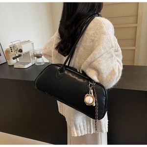 Detail of a black PU leather baguette bag with silver zippers and baseball charm