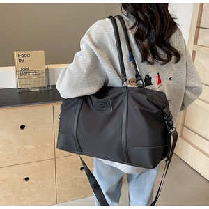 Detail view of large black nylon travel bag with shoulder strap and brand label