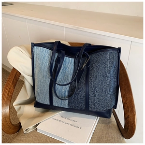 Detailed close-up of large blue denim patchwork tote bag with navy leather trim and handle
