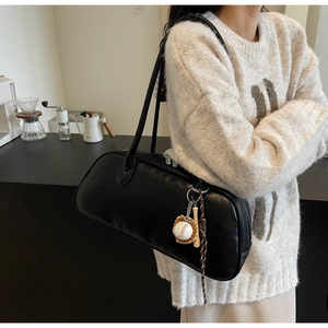 Detail of black leather cylindrical shoulder bag featuring creative baseball charms