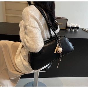 Detail of minimalist black leather baguette shoulder bag with baseball themed charm