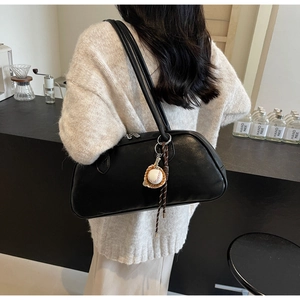 Detail of a black leather shoulder bag with a unique baseball charm on a café counter