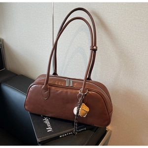 Close-up of caramel leather baguette bag with dual zippers and baseball pendant
