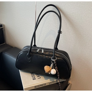 Close-up of black leather baguette bag with baseball charms on a minimalist book prop