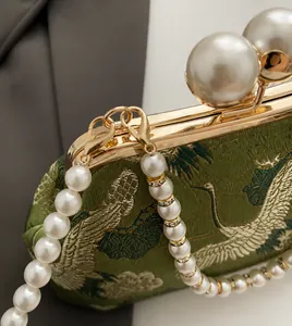 Close-up of emerald green embroidery with cranes and pearls on a silk evening bag