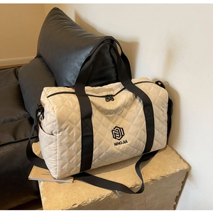 Dettaglio della borsa da viaggio beige trapuntata con motivi a rombi e tracolla nera