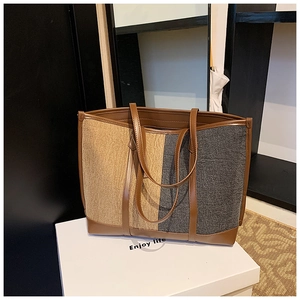 Detail of large canvas tote bag with contrast stitching and brown leather handles