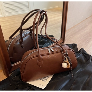 Detail of vintage brown leather baguette bag with unique baseball charm and long handles