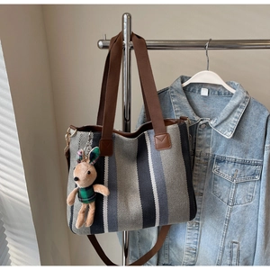 Detailed texture of blue striped canvas tote bag with brown straps and rabbit charm accessory