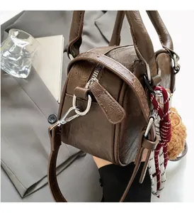 Close-up of vintage brown leather Boston bag featuring silver hardware and plush pendant