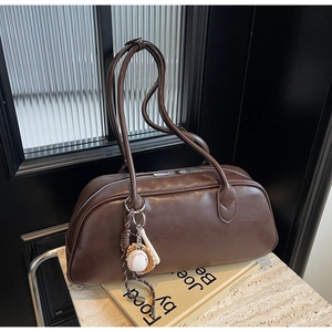 Detail of dark brown vintage shoulder bag with baseball charm on marble surface