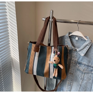 Detail of striped canvas tote bag with brown straps and a cute plush bunny charm