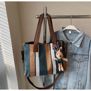 Detailed view of striped canvas tote bag with plush rabbit charm and shoulder strap