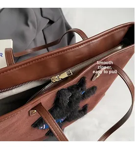 Close-up of golden metal zipper and plush cat patch on brown suede tote bag