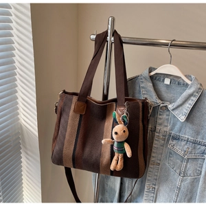 Brown striped canvas tote bag with a cute rabbit pendant hanging on a metal rack
