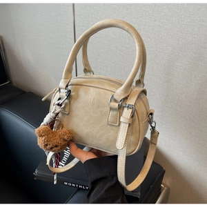 Detail of beige faux leather handbag with soft texture and cute brown teddy bear charm