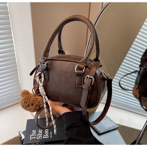 Close-up of vintage brown leather Boston bag with plush bear charm and woven cord detail