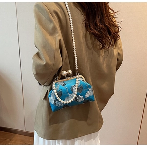 Detail of teal satin kiss-lock bag with crane pattern and elegant pearl chain strap