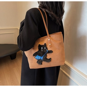 Detail of caramel tote bag featuring black cat embroidery and leather shoulder straps