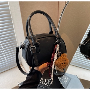 Close-up of black pebble leather satchel bag with plush bear charm and woven cord detail