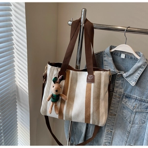 Detail of canvas tote bag featuring brown stripes, woven straps and a cute rabbit charm