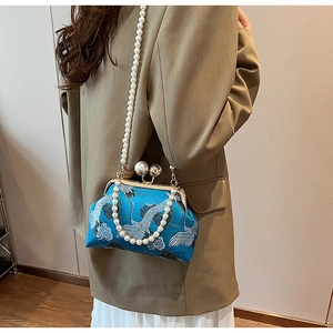 Detailed view of elegant blue brocade clutch with white crane embroidery and pearl strap