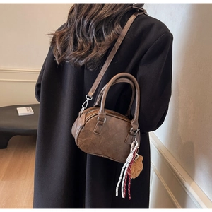 Deep brown retro Boston bag with plush bear charm worn by model in cozy interior