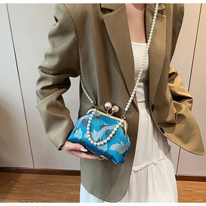 Close-up of blue satin evening bag with crane embroidery and pearl handle strap