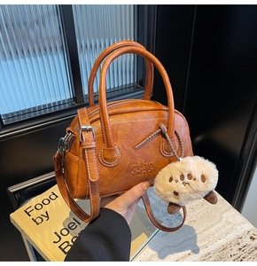 Nahaufnahme braune Lederhandtasche mit weißen Nähten und Plüsch-Anhänger