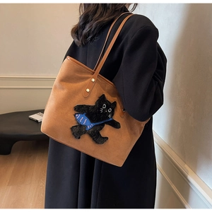 Detail of a brown suede tote bag featuring a 3D plush cat motif with a blue fish accessory