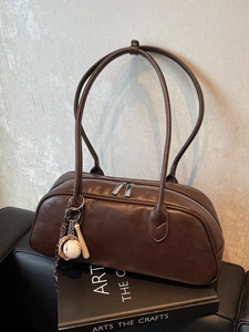 Vintage brown leather baguette shoulder bag with baseball charms on a minimalist background