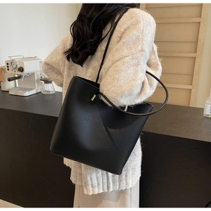 Detail of black pebbled leather tote bag with gold-tone hardware on a female model