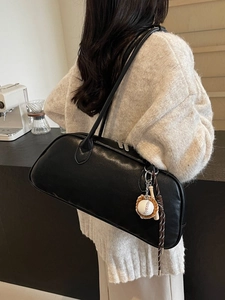 Minimalist black leather baguette shoulder bag with baseball charm on model
