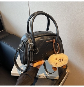 Detail der schwarzen Handtasche aus Narbenleder mit weißen Nähten und Plüsch-Anhänger