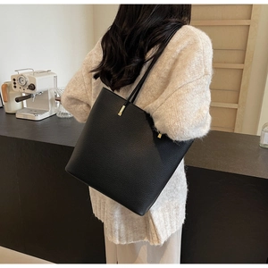 Detail of black litchi grain leather tote bag with gold hardware and slim shoulder strap