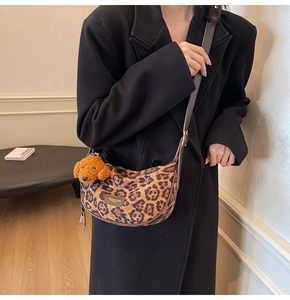 Detail view of leopard print crescent bag with plush teddy charm and brown leather trim