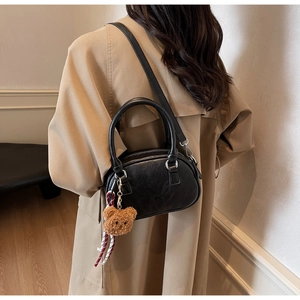 Model wearing a black leather Boston bag with a cute bear charm and striped ribbon detail