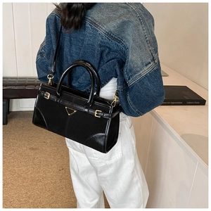 Detailed shot of black faux leather tote bag featuring gold triangular plaque and buckles