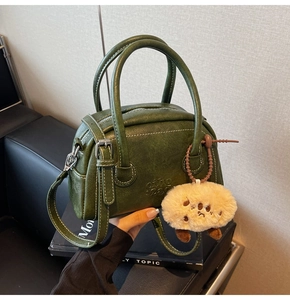Detail der dunkelgrünen Tasche mit Vintage-Textur, weißen Nähten und flauschigem Anhänger