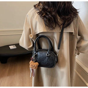 Rear view of black leather pillow bag with brown bear charm worn with khaki trench coat