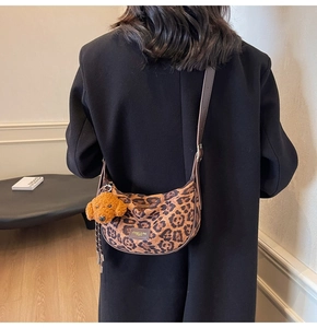 Detail of leopard print crossbody bag with brown leather tag and plush dog charm accessory