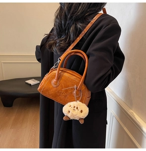 Detailaufnahme der orangebraunen Kissentasche mit Clio 2ad Prägung und Plüsch-Anhänger