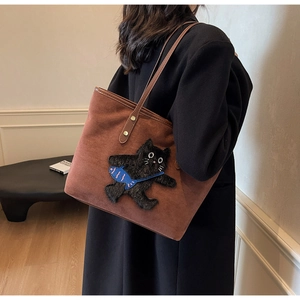 Detail of a brown suede tote bag with a whimsical black cat embroidery and gold rivets