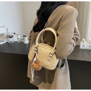 Detail of beige faux leather handbag with metal handle and cute plush bear charm