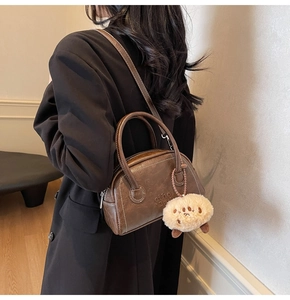 Nahaufnahme der braunen Boston-Tasche mit Plüsch-Anhänger an einem schwarzen Blazer