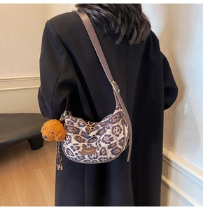 Detail of leopard print shoulder bag with leather trim and brown teddy bear charm on black coat