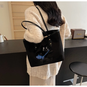 Close-up of a black canvas tote featuring a 3D plush cartoon cat with a blue fish bag