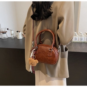 Brown vintage leather shoulder bag with teddy bear charm shown in a warm lifestyle setting
