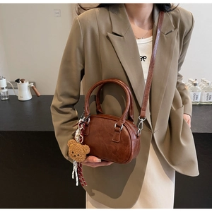 Detail of dark brown vintage PU leather satchel with cute plush bear charm on side