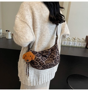 Detail of leopard print crescent bag with plush puppy charm and adjustable strap